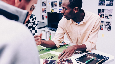 Man talking to two other men over creative papers